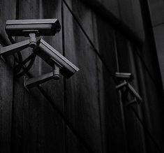 two security cameras mounted to the side of a wooden building with wires running through it