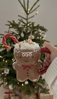 a person holding a mug with a frosted gingerbread in front of a christmas tree