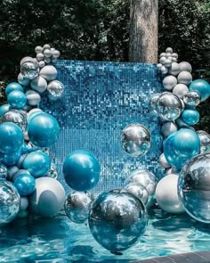 blue and silver balloons floating in the water near trees with bubbles on them, as well as other decorations