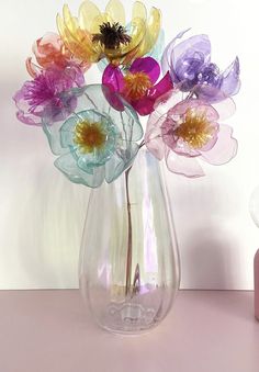 a vase filled with colorful flowers sitting on top of a pink table next to a light bulb