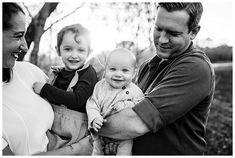 a black and white photo of a man holding a baby in his arms while two other people look on