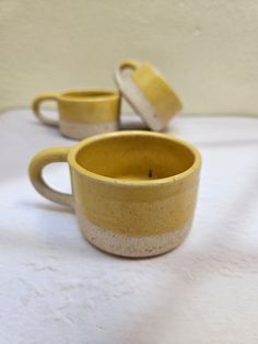 two yellow cups sitting on top of a white tablecloth next to each other with one cup in the middle