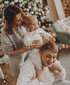 a man holding a baby in his arms while sitting next to a woman and christmas tree