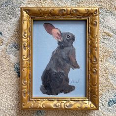 a painting of a rabbit in a gold frame on the floor next to a carpet