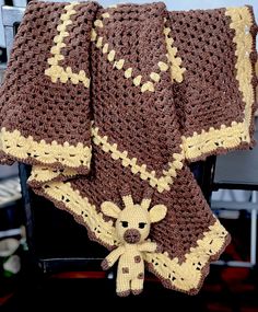 a crocheted blanket with a teddy bear on it sitting next to a chair