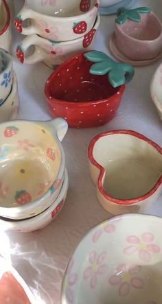 a table topped with bowls and plates covered in strawberry design dishes on top of a white cloth