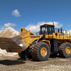 a large yellow construction vehicle parked on top of a dirt covered field with mountains in the background