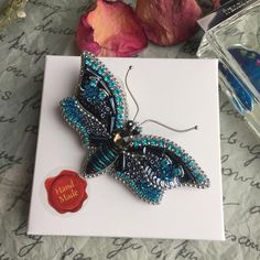 a blue butterfly brooch sitting on top of a card next to some pink flowers