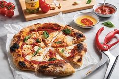 a pizza sitting on top of a cutting board next to some sauces and tomatoes