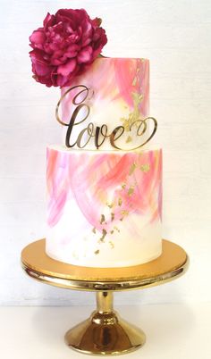 a three tiered cake with pink and gold decorations on the top, topped with a flower