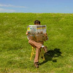 a man sitting in a chair reading a newspaper on top of a lush green field