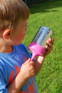 a young boy holding a pink hair dryer in his right hand and looking at the grass