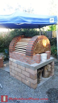 an outdoor brick pizza oven sitting under a blue tarp