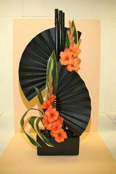 an arrangement of flowers in a black vase with fan shaped decoration on the top and bottom