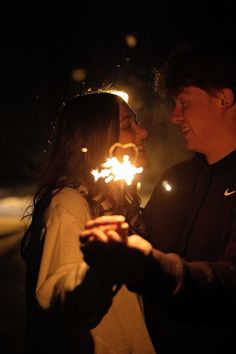 two people standing next to each other holding sparklers in their hands and looking at each other