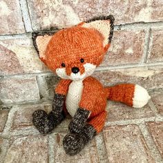 a knitted stuffed fox sitting on top of a stone floor next to a brick wall