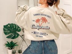 This cool retro California sweatshirt with palm trees design is the perfect gift idea or souvenir for every surfer in summer. Get yours now! Also available on t-shirts: https://www.etsy.com/listing/1044201694/retro-california-tee-california-tshirt Browse through my other awesome items here: http://thenims.etsy.com/ ABOUT THE PRODUCT: Unisex Heavy Blend™ Crewneck Sweatshirt | GILDAN 18000 (Customer Favorite) A sturdy and warm sweatshirt bound to keep you warm in the colder months. A pre-shrunk, c Trendy Summer Leisure Sweatshirt, Summer Short Sleeve Relaxed Fit Sweatshirt, Relaxed Fit Short Sleeve Sweatshirt For Summer, Casual Crew Neck Top With Palm Tree Print, Trendy Summer Sweatshirt With Letter Print, Trendy Summer Sweatshirt With Text Print, Summer Crew Neck Sweatshirt With Graphic Print, Trendy Graphic Print Sweatshirt For Vacation, Oversized Summer Sweatshirt With Graphic Print