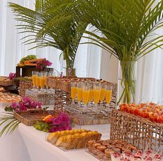 an assortment of food and drinks displayed on a buffet table with palm trees in the background