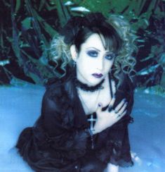 a woman sitting in the snow with her hands on her chest and wearing black clothes