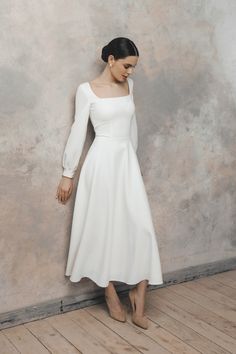 a woman in a white dress leaning against a wall