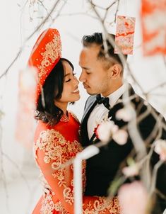 a bride and groom standing in front of a tree at their wedding ceremony with red flowers on the branches