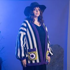 a woman standing in front of a blue background wearing a black hat and striped cardigan