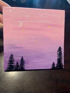 someone is holding up a small canvas with trees on it and the moon in the sky