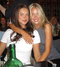 two beautiful young women sitting next to each other at a table with bottles and glasses