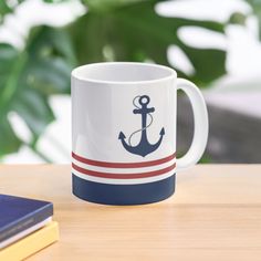 a coffee mug with an anchor on it sitting on a table next to a book