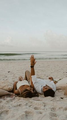 a man laying on top of a sandy beach next to the ocean with his hands in the air