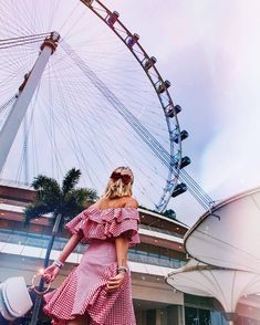 a woman in a red and white dress standing next to a ferris wheel with sunglasses on