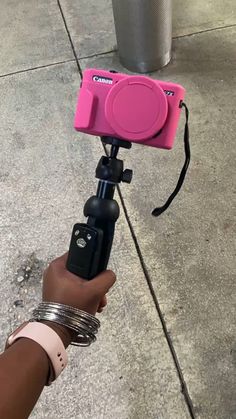 a person holding a pink camera on top of a tripod in front of a pole