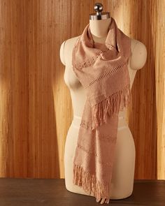 a mannequin wearing a pink scarf on top of a wooden table in front of a wood paneled wall