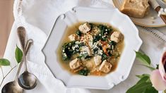 a white bowl filled with soup and meat on top of a table next to bread