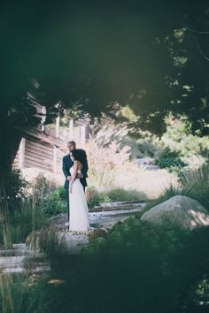 a bride and groom standing in front of a house surrounded by greenery at their wedding