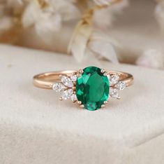 an emerald and diamond ring sitting on top of a white flowered cloth with flowers in the background