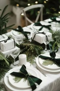 the table is set with white plates and green ribboned napkins, silverware, greenery and candlesticks