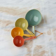 three colorful measuring spoons sitting on top of a marble counter next to each other