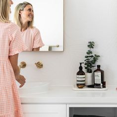 two women standing in front of a bathroom mirror looking at each other's reflection