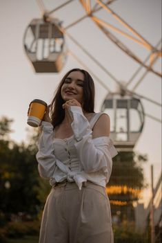 a woman standing in front of a ferris wheel holding a coffee cup