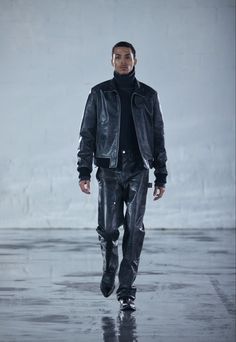 a man in black jacket and pants walking down a runway