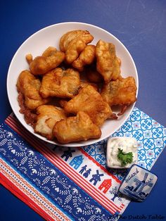 a white plate topped with fried food next to a blue and red table cloth on top of a wooden table