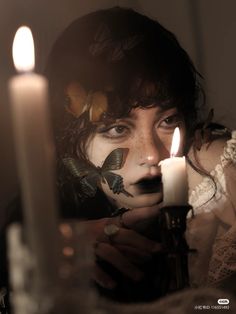 a woman holding a candle in front of her face with butterflies painted on her face