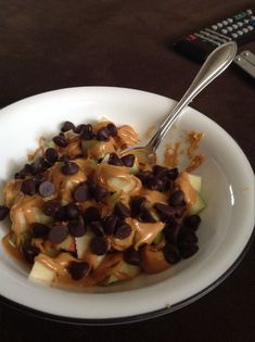 a white bowl filled with chocolate chips and caramel sauce next to a remote control