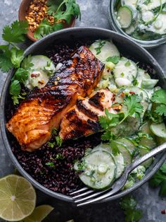 a bowl filled with black rice, cucumber and salmon on top of it