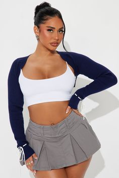 a woman wearing a white crop top and grey skirt with her hands on her hips