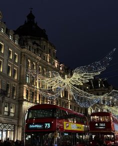 a double decker bus parked in front of a building with christmas lights hanging from it's sides