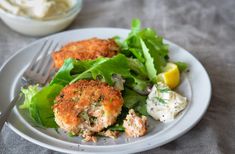 two crab cakes on a plate with lettuce, lemon wedges and mayonnaise