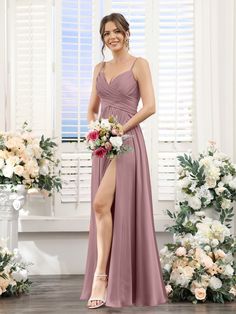 a woman in a long dress standing next to some flowers and holding a flower bouquet