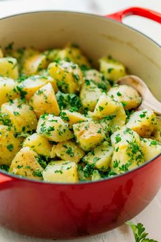 a red pot filled with potatoes and parsley on top of a white tablecloth